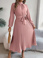 Woman wearing a pink dress with a belt in a room with a couch and plant.