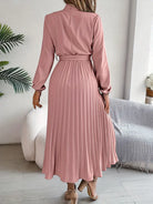 Woman wearing a pink pleated dress in a room with a couch and plant.