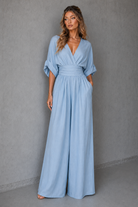 Woman wearing a light blue jumpsuit against a gray background