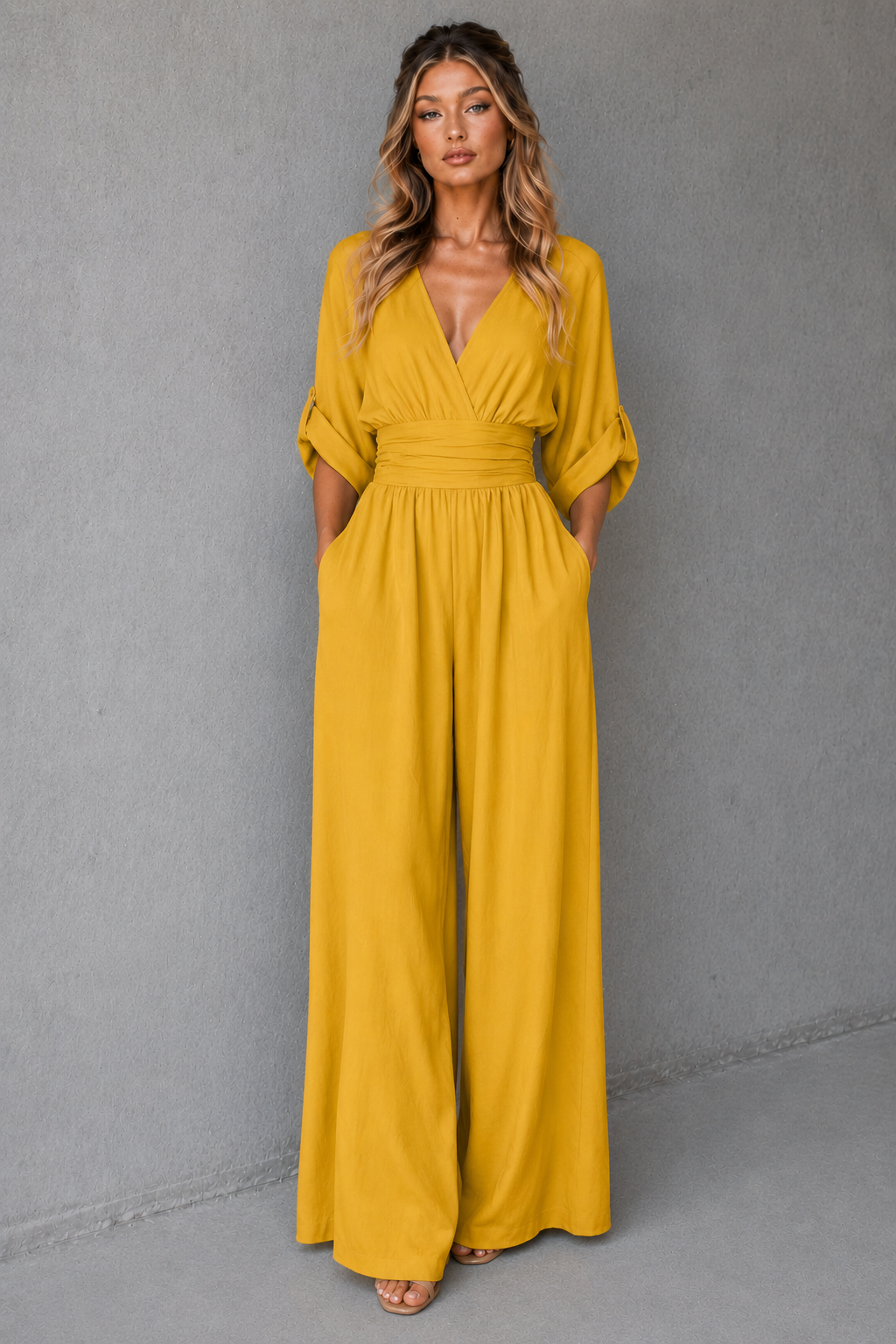 Woman wearing a mustard yellow jumpsuit against a gray background
