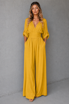Woman wearing a mustard yellow jumpsuit against a gray background