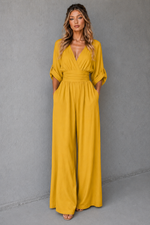 Woman wearing a mustard yellow jumpsuit against a gray background