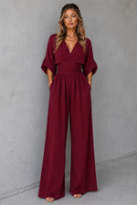 Woman wearing a burgundy jumpsuit against a gray background