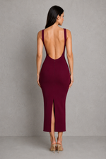 Woman wearing a burgundy dress with an open back and slit on a gray background