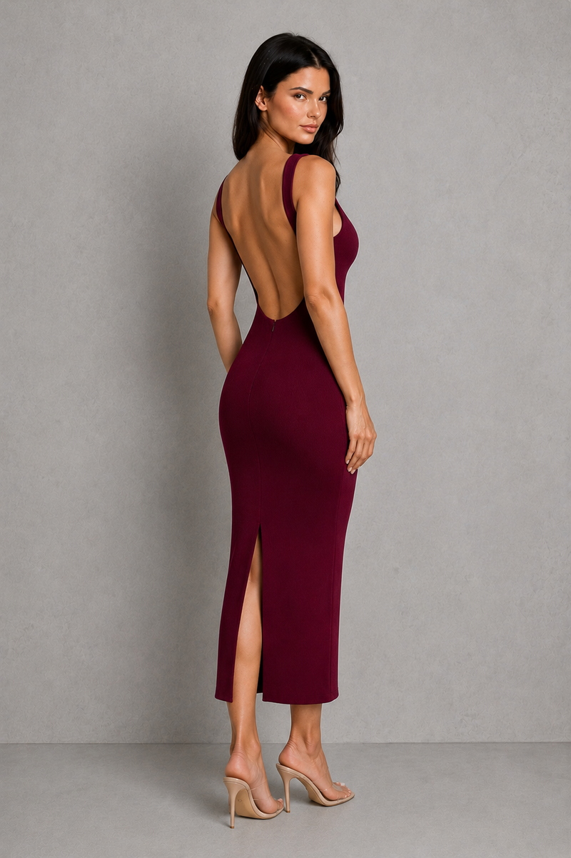 Woman wearing a burgundy dress with an open back and slit on a gray background