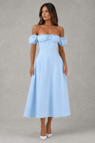 Woman wearing a light blue off-shoulder dress against a gray background