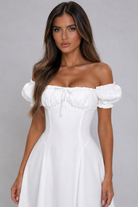 Woman wearing a white off-shoulder dress against a gray background