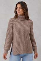 Woman wearing a brown knitted turtleneck sweater against a plain background