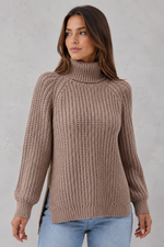 Woman wearing a brown knitted turtleneck sweater against a plain background