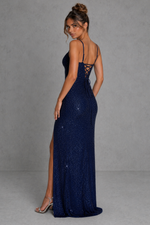 Woman wearing a navy blue evening gown with a high slit on a gray background
