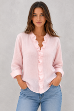 Woman wearing a pink ruffled blouse and blue jeans against a gray background