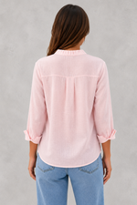 Woman wearing a light pink blouse and blue jeans against a gray background