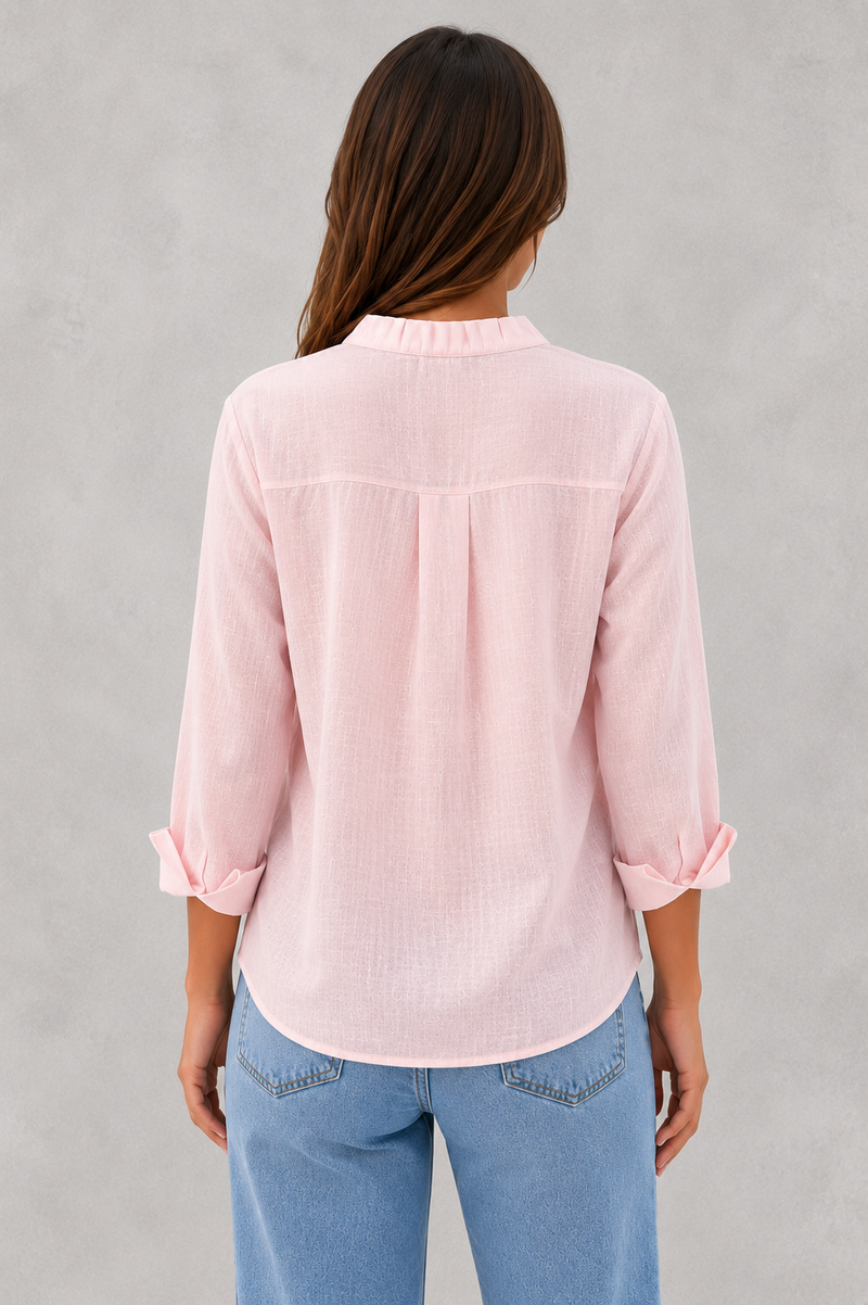 Woman wearing a light pink blouse and blue jeans against a gray background