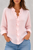 Person wearing a pink ruffled blouse and blue jeans on a gray background