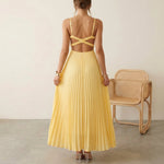 Woman wearing a yellow pleated dress with a chair in the background