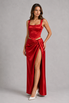 Woman wearing a red satin dress with a slit on a gray background