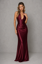 Woman wearing a burgundy satin evening gown against a gray background