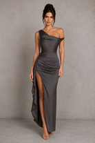 Woman wearing a gray one-shoulder dress with a high slit on a plain background