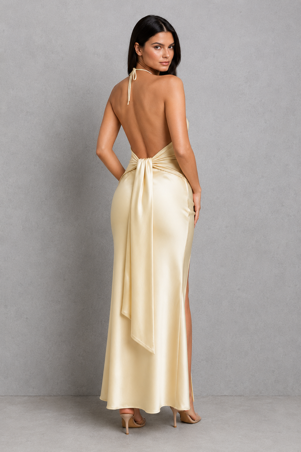 Woman wearing a light yellow evening gown with a backless design on a gray background