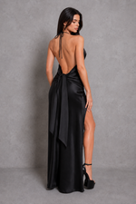 Woman wearing a black satin evening gown with a high slit on a gray background