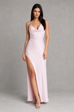 Woman wearing a light pink evening gown with a high slit on a gray background