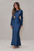 Woman wearing a blue evening gown with cut-out design on a plain background