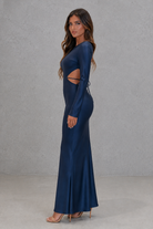 Woman wearing a blue evening gown with cut-out design against a gray background