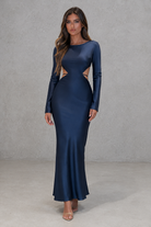 Woman wearing a long-sleeve navy dress with cut-out design against a gray background