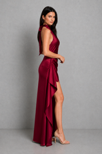 Woman wearing a burgundy evening gown with a slit on a gray background