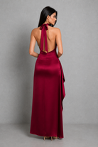 Woman wearing a burgundy evening gown with a halter neck design against a gray background