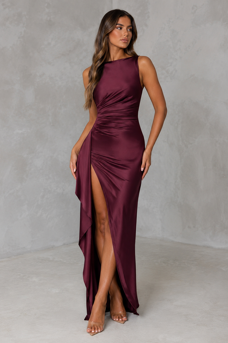 Woman wearing a burgundy dress with a high slit on a plain background