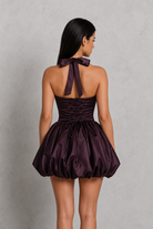 Woman wearing a purple dress with a bow detail on a gray background