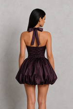 Woman wearing a purple dress with a bow detail on a gray background