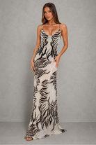 A woman modeling a floor-length slip gown with a black and off-white zebra print against a textured gray studio backdrop.