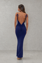 Woman wearing a blue evening gown with a open back against a gray background