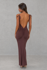 Woman wearing a brown dress with open back against a gray background
