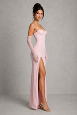 Woman wearing a pink evening gown with a high slit and long gloves against a gray background