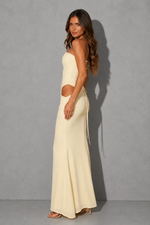 A woman modeling a cream-colored two-piece set consisting of a strapless crop top and a matching high-waisted maxi skirt with side cutouts and tie details, set against a gray studio background.