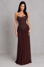 Woman wearing a strapless brown evening gown with a textured bodice on a gray background