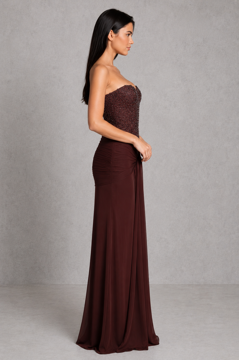 Woman wearing a strapless brown evening gown against a plain background