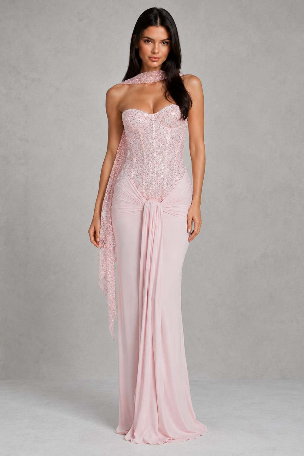 Woman wearing a pink strapless gown with a sheer overlay against a gray background