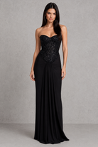 Woman wearing a black strapless gown with sequin detailing on a gray background