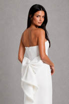 Woman wearing a white strapless dress with a large bow on a gray background