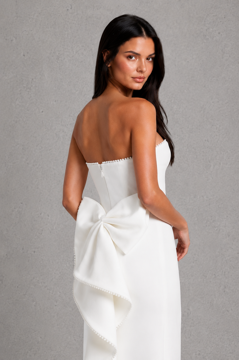 Woman wearing a white strapless dress with a large bow on a gray background