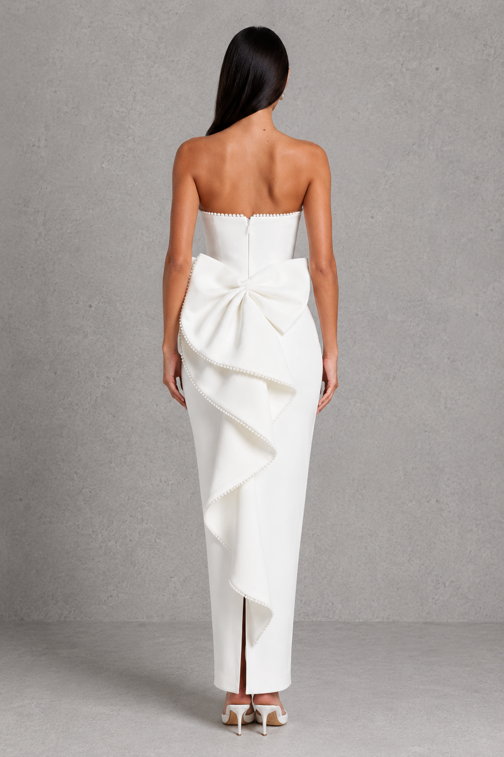 Woman wearing a white strapless gown with a large bow detail on a gray background
