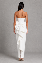Woman wearing a white strapless gown with a large bow detail on a gray background