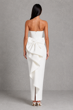 Woman wearing a white strapless gown with a large bow detail on a gray background