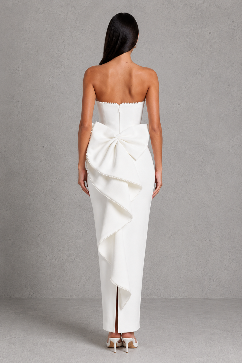 Woman wearing a white strapless gown with a large bow detail on a gray background