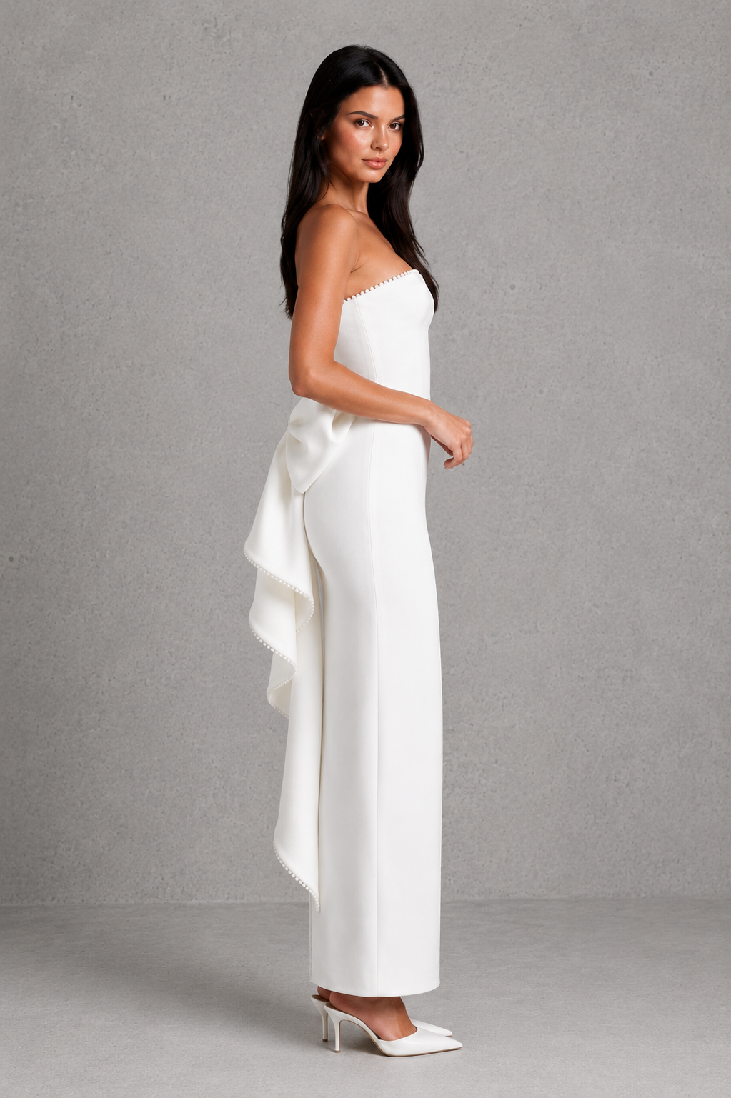 Woman wearing a white strapless jumpsuit with a bow detail on a gray background
