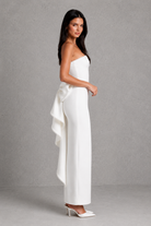 Woman wearing a white strapless jumpsuit with a bow detail on a gray background